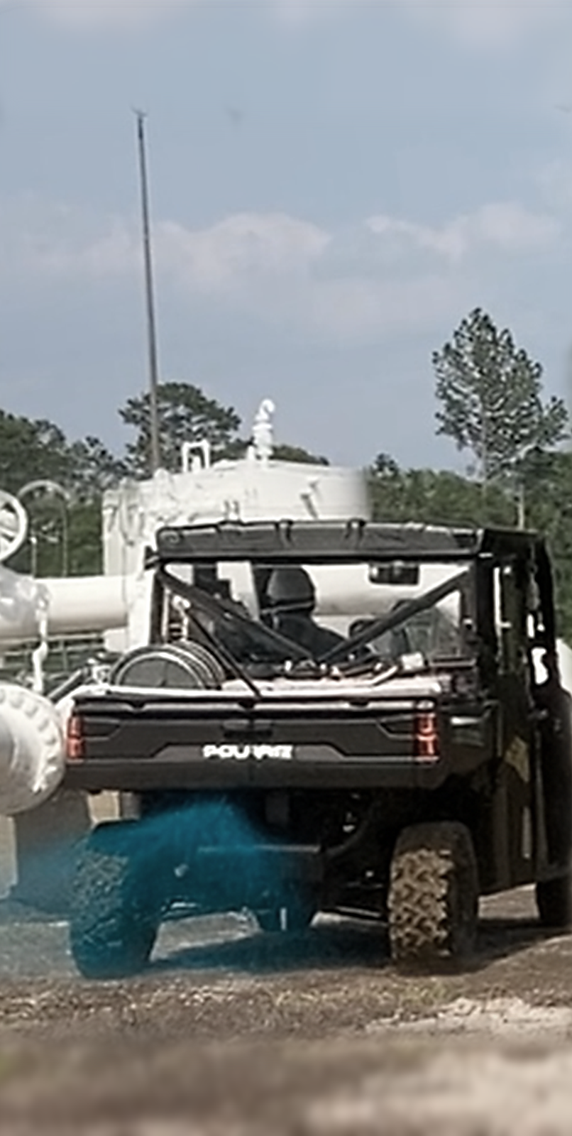 Polaris side-by-side spray rig applying blue herbicide for industrial and commercial weed control, equipped with hose reel, tank, and boomless nozzle setup. Ideal for vegetation management services on large industrial sites, utility facilities, and commercial properties where precision application and reliable equipment maintenance are essential for effective weed elimination.