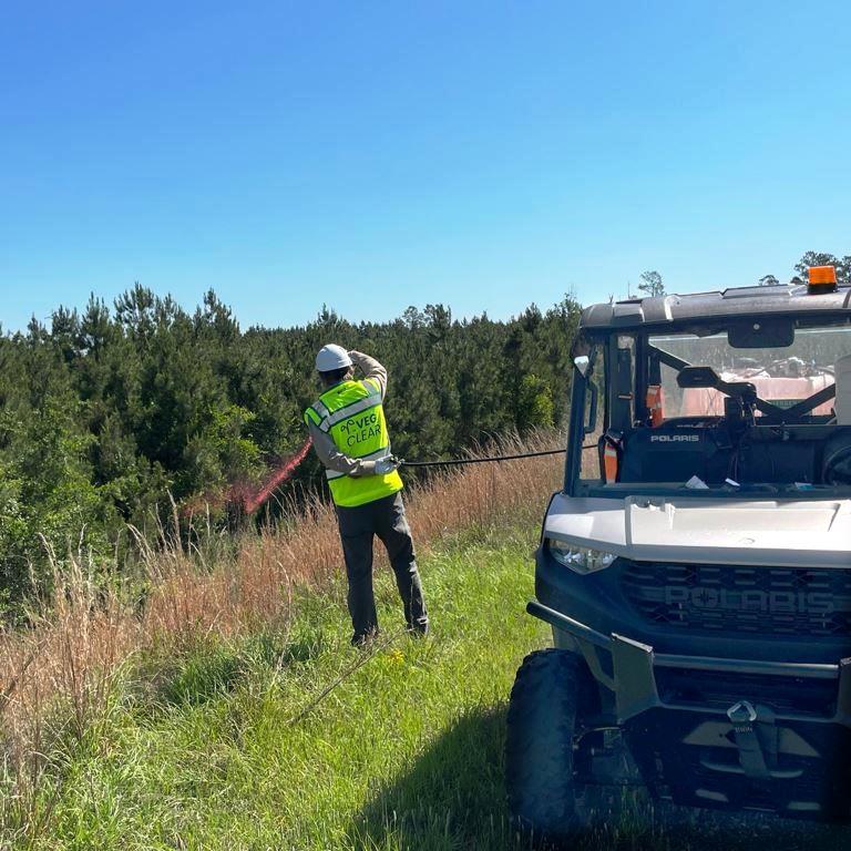 VegClear technician performing selective vegetation management and brush control on an industrial hillside using a Polaris ATV sprayer system. Licensed herbicide application for utility, municipal, and industrial right-of-way maintenance.