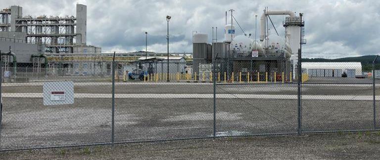 Industrial chemical plant facility with fenced gravel yard and critical equipment area needing brush and vegetation control to maintain access, safety, and visibility for operations, utilities, and inspections.