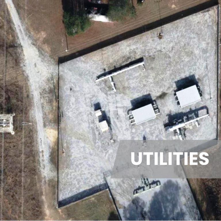 Aerial view of an electric utility substation with gravel yard, equipment pads, access roads, and perimeter areas managed for vegetation control and compliance
