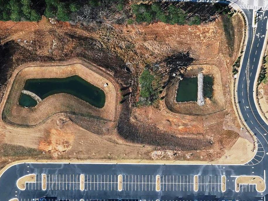 Aerial view of commercial retention ponds and stormwater basins beside paved access roads, maintained through vegetation control to support drainage performance, slope stability, inspections, and long term site compliance.