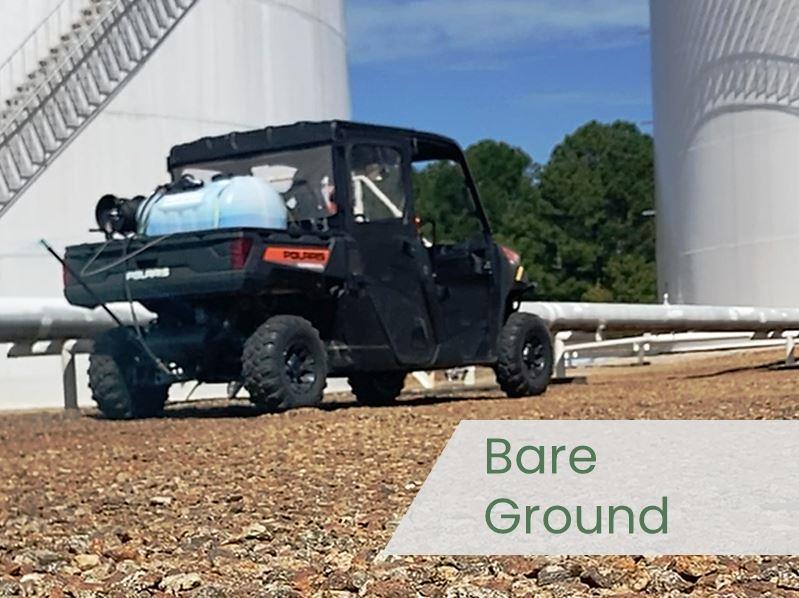 Side by side utility vehicle with a skid sprayer applying bare ground herbicide on gravel at an industrial tank farm to maintain weed free surfaces.