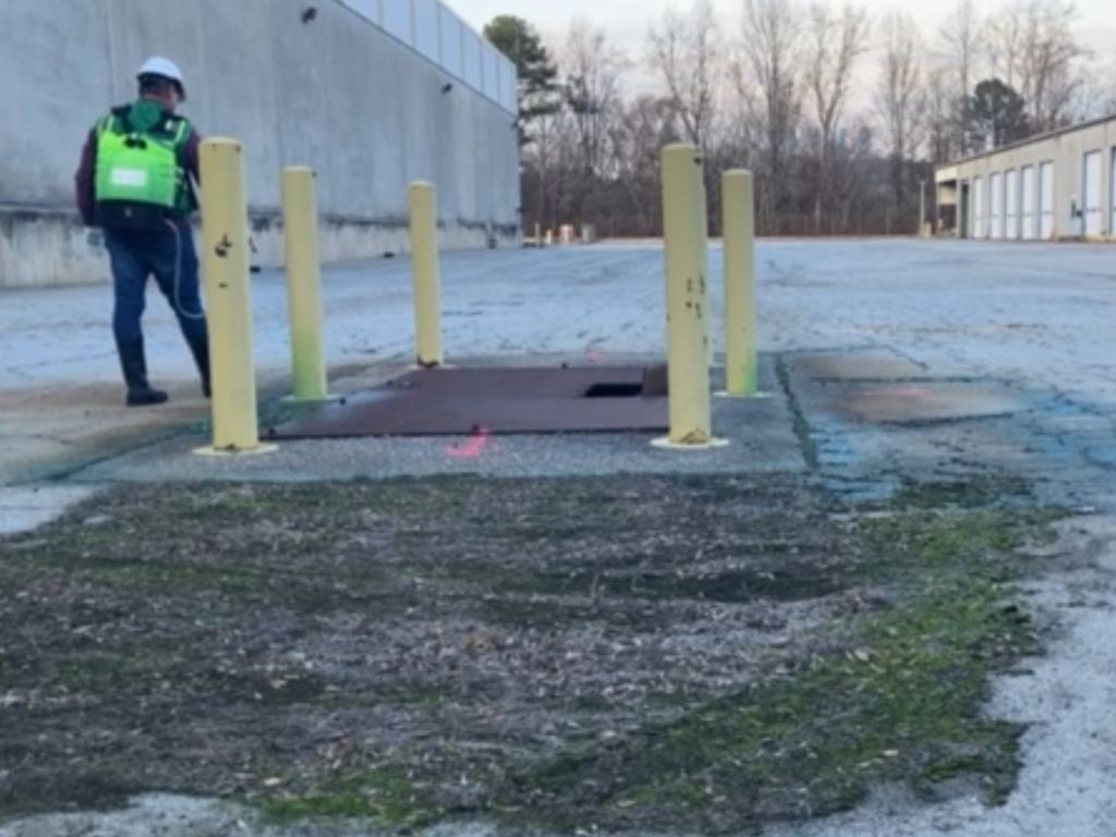 VegClear partner and director of operations performing precision herbicide treatment around pavement fixture bases and bollards at an industrial facility, demonstrating controlled bare ground vegetation management in a commercial operations environment.