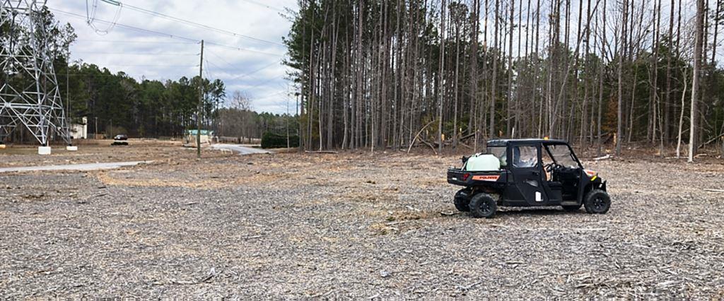 UTV spray rig positioned on cleared industrial site near transmission lines. Represents professional vegetation management contractors providing brush control and site clearing for utility infrastructure.