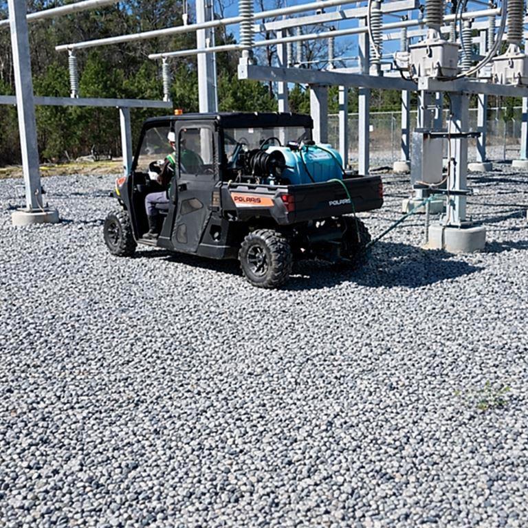 Industrial vegetation management at electrical substation with gravel surface and utility terrain vehicle applying bareground herbicide treatment for long term weed control and site compliance.