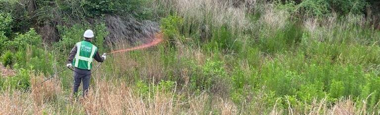 VegClear technician performing selective brush control and woody vegetation treatment on an overgrown industrial hillside using directed herbicide applications for long-term vegetation management.
