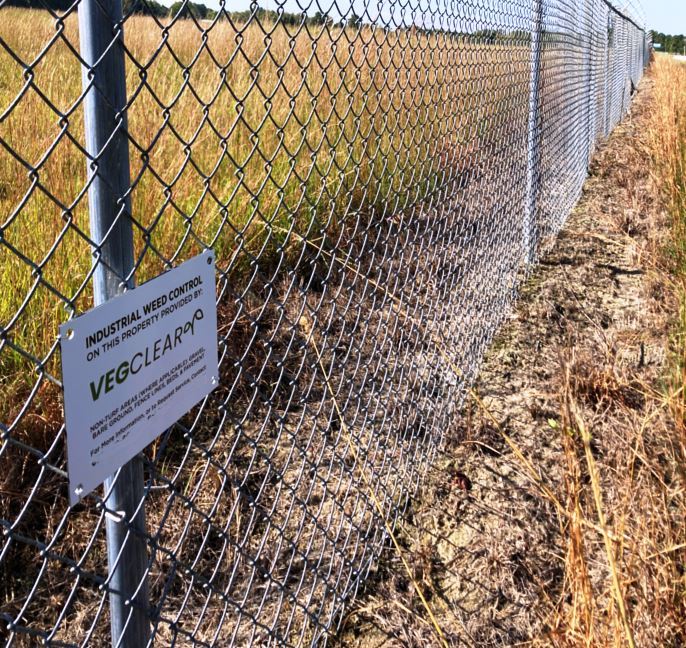 Commercial and retail property overgrown with weeds with fuel pump canopy, requiring spraying cracks and weeds along curbs and across parking areas by VegClear