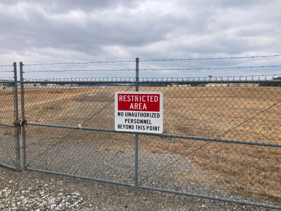 Restricted area gate marking controlled access to airport operations zones requiring compliant vegetation management.