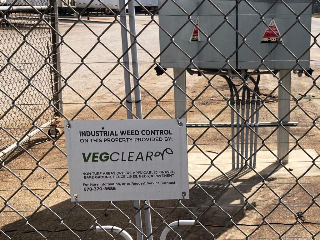 VegClear industrial weed control sign mounted on chain link fence at a non turf utility site, indicating managed gravel, bare ground, and fence line vegetation control in Georgia.