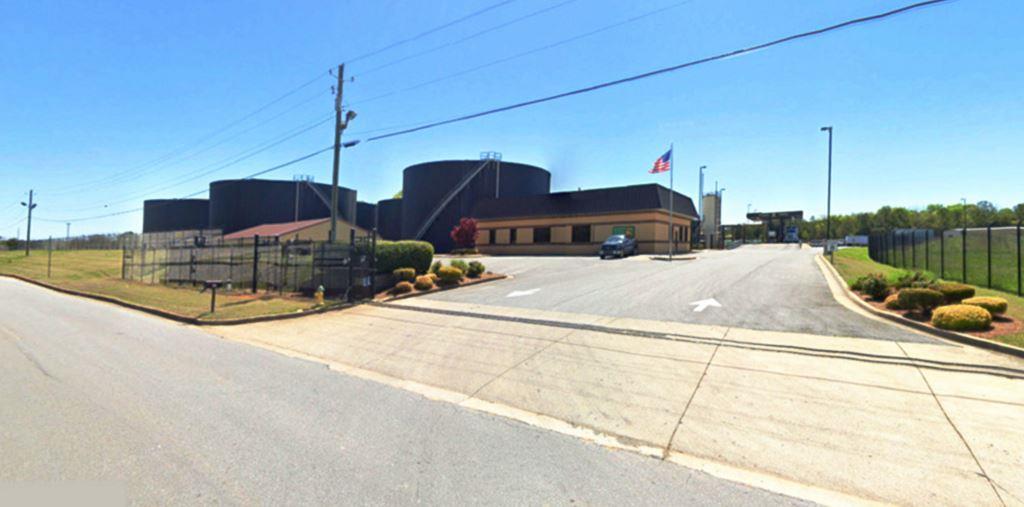 Commercial vegetation control site showing hybrid industrial property with large tank storage, warehouse buildings, and fenced perimeters requiring herbicide weed management in Georgia.