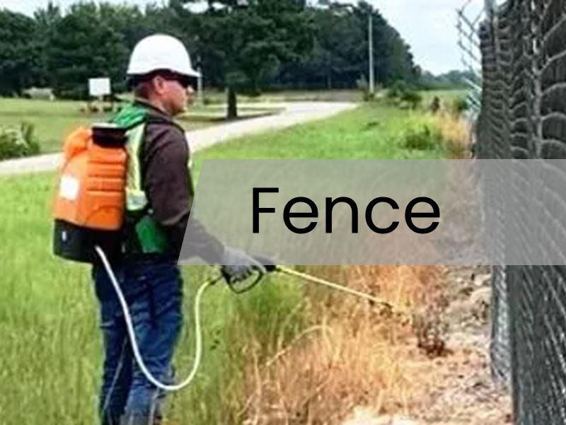 Tech spraying herbicide along commercial fence line for vegetation control and weed management.