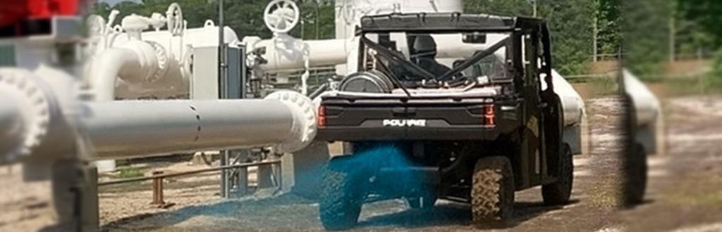 Utility vehicle spraying blue herbicide at an energy facility to control weeds and invasive plants. VegClear provides licensed herbicide applications for industrial vegetation management, ensuring compliance and safety across pipelines, utilities, and facilities.