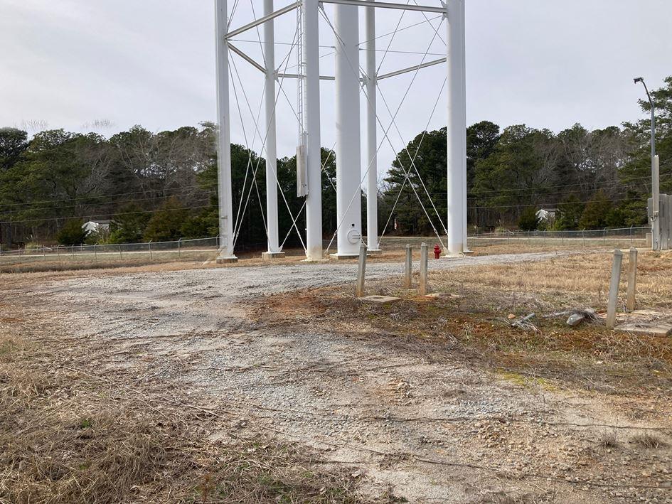 Gravel access road and managed perimeter beneath a municipal water tower, showing non turf industrial vegetation control on utility property in Georgia.