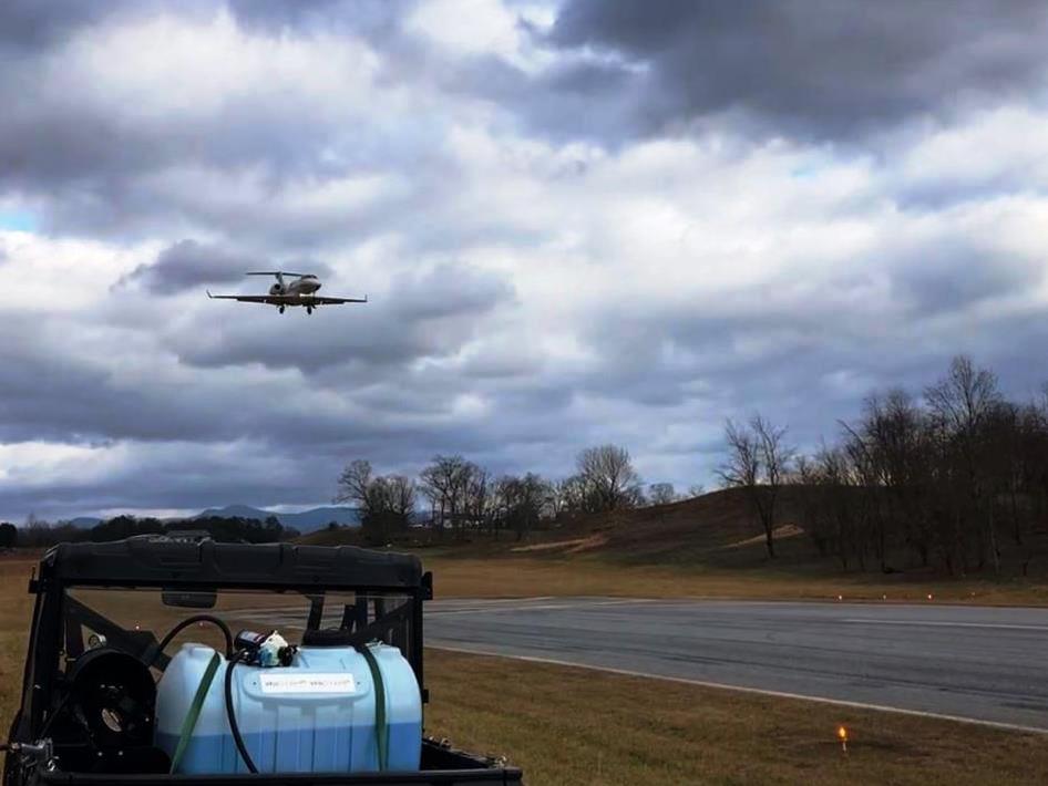 VegClear spray rig beside active runway with landing aircraft, reflecting coordinated vegetation control operations.