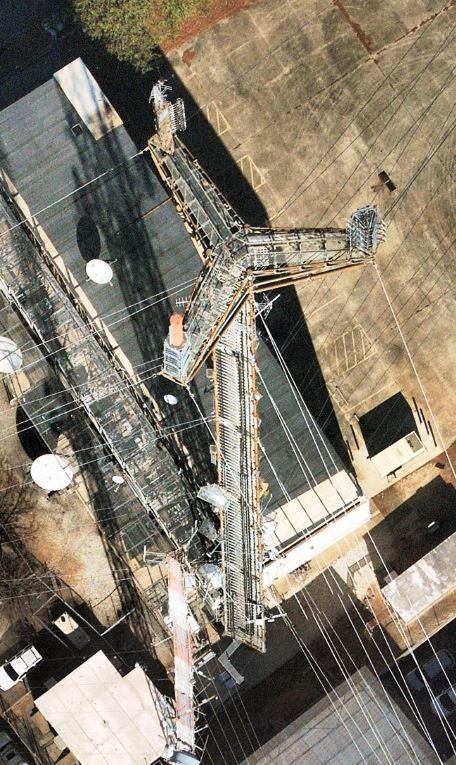 An action shot of licensed VegClear technicians wearing protective gear as they apply non-selective liquid herbicides using backpack sprayers along the fence lines and gravel areas of a BearCom communication tower site. The workers are meticulously treating areas around critical Motorola communication equipment to prevent vegetation resurgence. The image emphasizes the precision and care taken to maintain vegetation-free zones essential for optimal performance of Motorola's advanced communication systems, ensuring reliable connectivity for public safety and enterprise operations.