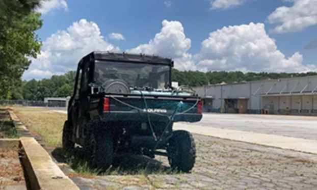 VegClear side-by-side sprayer parked along an industrial pavement edge performing total vegetation control for commercial hardscape and curb areas using non-selective herbicide on overgrown surfaces