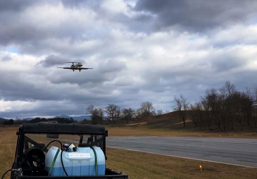VegClear spray rig staged beside municipal runway with aircraft landing, showing active vegetation control operations at a Georgia airport.