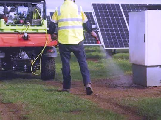 Technician Applying Herbicide to Manage Vegetation Around Solar Panels at a Farm Site