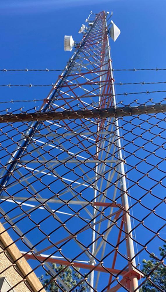 Cell tower surrounded by cleared vegetation and bare ground, showing results of herbicide-based vegetation management to maintain safe, accessible tower site; image supports tower maintenance, utility vegetation control, and RF compliance keyword relevance for VegClear's services.
