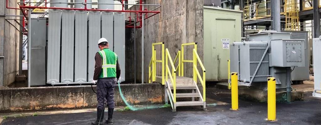 Licensed applicator performing pavement weed control with herbicide along concrete pad at an industrial power substation in Georgia.
