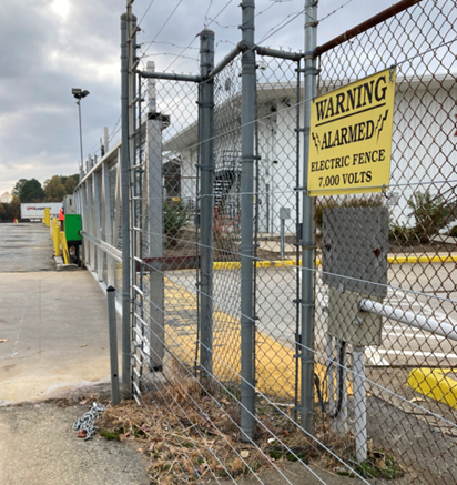 Distribution Hub with Electric Security Fence – Vegetation Management: Industrial distribution hub with an electric security fence and chain-link barrier, kept clear with precision herbicide treatments. Effective weed control prevents vegetation interference and enhances perimeter security.