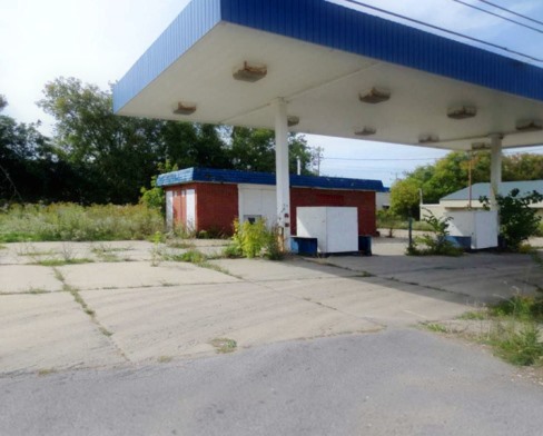 Commercial and retail property overgrown with weeds with fuel pump canopy, requiring spraying cracks and weeds along curbs and across parking areas by VegClear