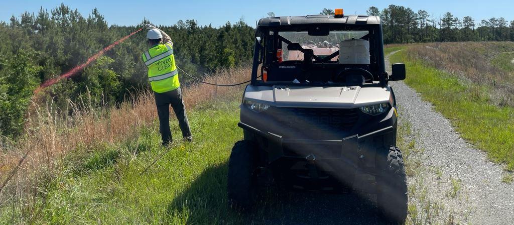 VegClear technician performing selective brush and fence line herbicide treatment along an airport perimeter access road using ATV spray equipment in an active aviation environment.