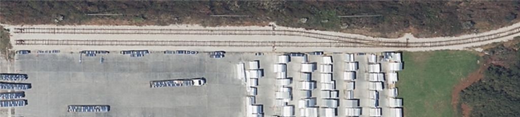 Aerial view of an industrial facility with active rail spur, trailer storage, and concrete staging area, surrounded by turf and unmanaged edges—ideal candidate for VegClear’s industrial vegetation control services. Targeted herbicide application prevents overgrowth along fence lines, loading zones, and rail infrastructure across Southeastern logistics and distribution sites.