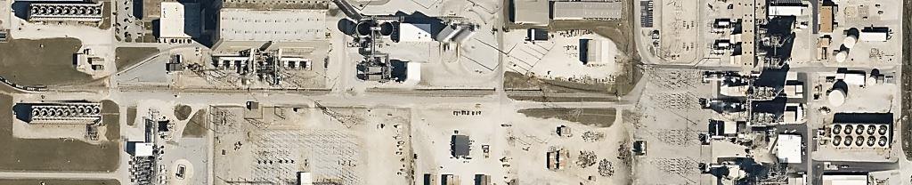 Aerial view of a large industrial utility facility with power generation infrastructure, storage tanks, cooling towers, and gravel-covered work areas. Highlights the scope of industrial vegetation management and weed control services needed to maintain clear, safe, and compliant operations across expansive facility grounds.