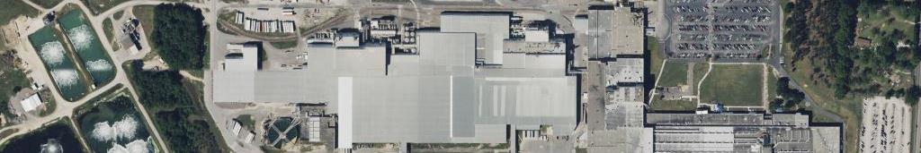 Aerial view of a large industrial manufacturing facility with paved lots, equipment yards, retention ponds, and perimeter grounds requiring brush control, vegetation management, and right-of-way maintenance.