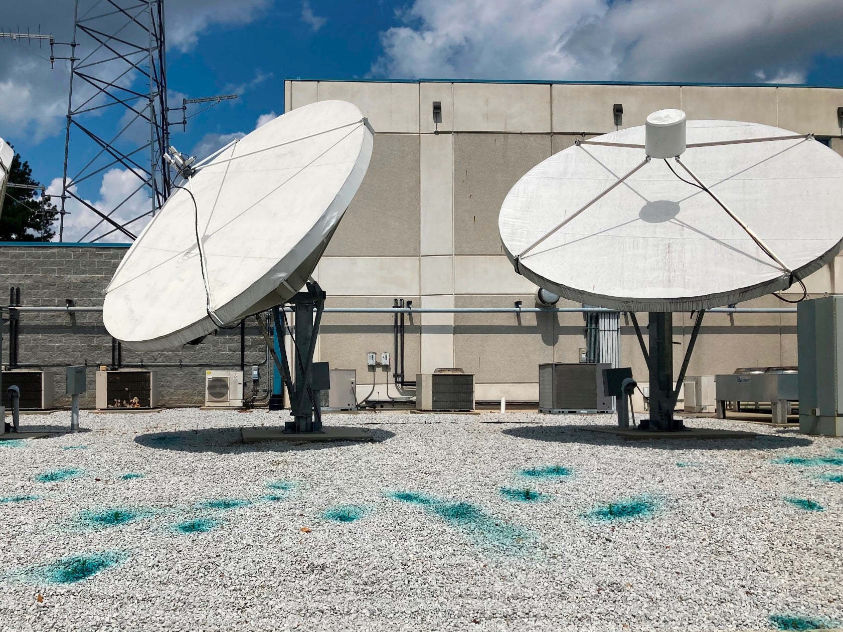 Satellite dishes mounted on a gravel rooftop at an industrial facility, illustrating non turf vegetation control zones and the importance of managing gravel surfaces to prevent weed growth around critical communications infrastructure.