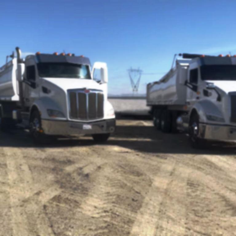 Industrial spray trucks staged on a gravel landfill access road, illustrating large scale herbicide application capability and equipment access required for landfill vegetation management and non turf weed control operations
