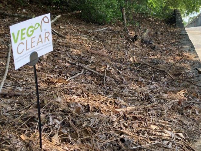 VegClear treatment site at a Norcross, GA self storage facility cleared retaining wall and slope. A sign indicates completed herbicide application near storage units, concrete surfaces, and perimeter areas