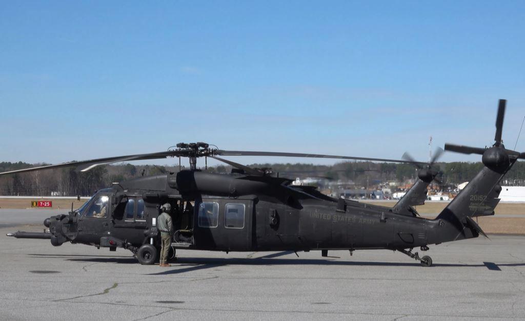 Military Black Hawk helicopter positioned on an active airfield apron near aviation infrastructure and secured operational areas associated with military airport and airfield facility management.
