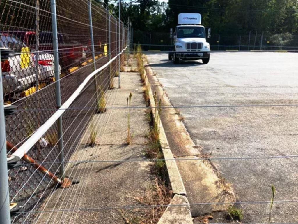 VegClear industrial weed control treatment along a fenced logistics yard in Georgia. Targeted herbicide application eliminates weeds along pavement and barriers for safer, low-maintenance property operations.