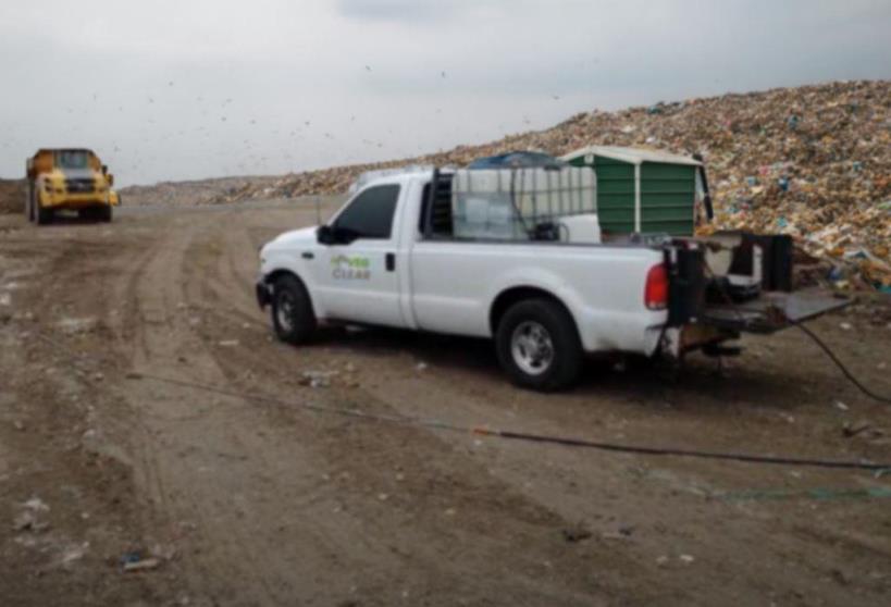 VegClear vegetation control spray truck with mounted herbicide tank at an active landfill site, demonstrating industrial vegetation management for waste facility perimeters and debris-covered access roads. Image shows rugged landfill terrain, heavy equipment, and targeted weed control operations.