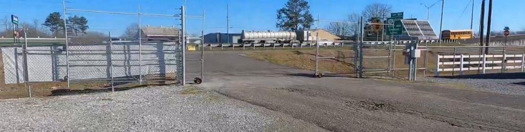 Secure fenced access gate at an industrial facility with visible gravel lot and clear fence lines, showing pre-treatment conditions for industrial weed control near highways in Georgia.