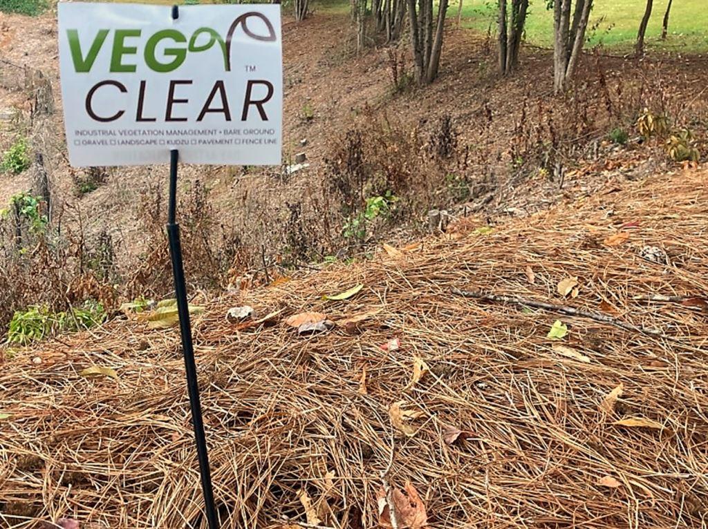 VegClear sign posted on a treated hillside showing bare ground and suppressed vegetation after herbicide based integrated vegetation management. Represents industrial weed control, slope safety, and long term vegetation suppression.