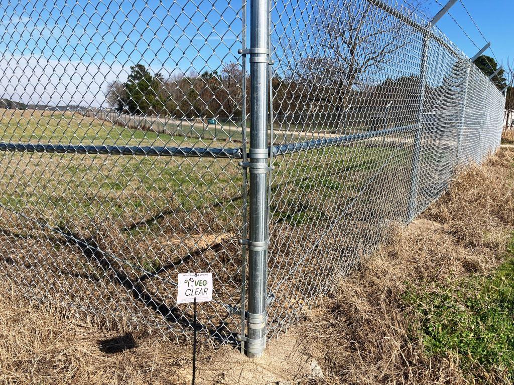 Chain link security fence at an industrial site with treated bare ground perimeter and dormant grass. Example of professional fence line vegetation control for access, visibility, and long term perimeter maintenance.